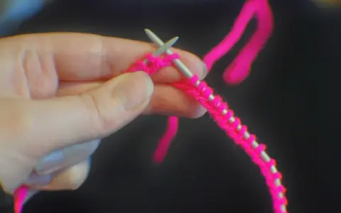 En hand håller stickor och ljusrosa garn, redo att starta stickning.