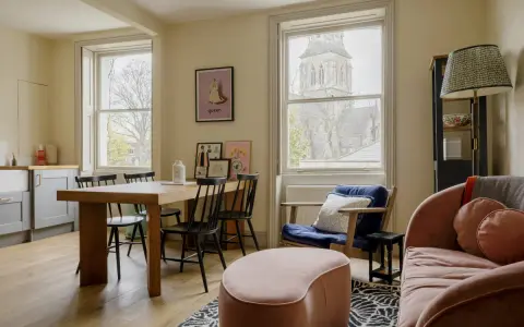 Idee soggiorno piccolo con divano rosa e tavolo in legno. Arredamento accogliente con sedie nere e pouf bombato.