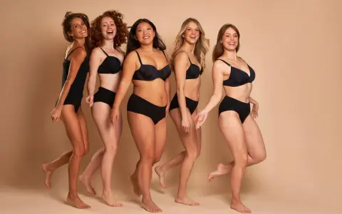 Cinque donne diverse, con taglia nona di seno e forme varie, camminano sorridenti in lingerie nera.