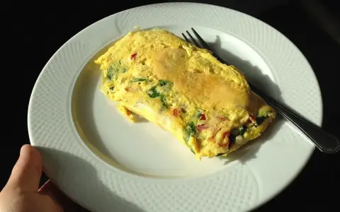 Pyszne śniadanie na redukcji: omlet z warzywami na białym talerzu, gotowy do zjedzenia.