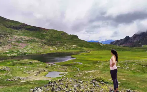 Mujer admira un lago y prados verdes en el Valle de Tena, ideal para rutas de senderismo.
