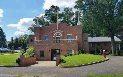 The Holy Face Monastery, a brick building with a large cross, stands on a sunny day.