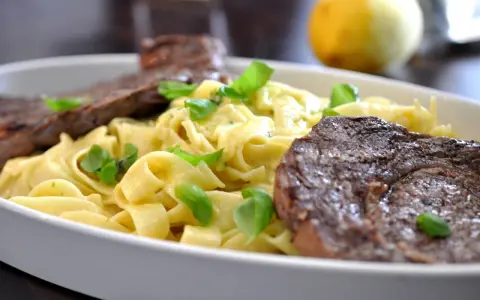 En krämig pastarätt med tagliatelle, garnerad med färsk basilika och serverad med saftig entrecote.
