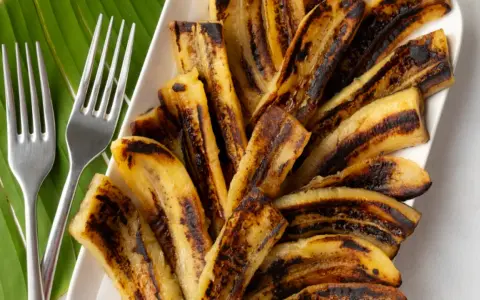 Bananes flambées grillées sur une feuille de bananier, prêtes à être dégustées avec deux fourchettes.