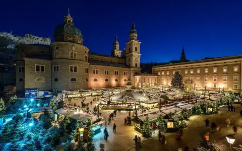 A magical Salzburg Austria Christmas market glows at night, with stalls, trees, and the cathedral creating a festive scene.