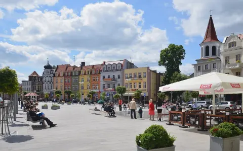 Kolorowy brodnica rynek tętni życiem. Ludzie odpoczywają na ławkach, a kawiarniany ogródek zaprasza do relaksu pod białym parasolem.