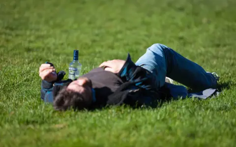 Mężczyzna leży na trawie obok butelki wódki. Czy padaczka alkoholowa jest śmiertelna? To pytanie budzi niepokój.
