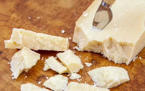 Kawałki Grana Padano na drewnianej desce, gotowe do posypania makaronu lub dodania do sosów.