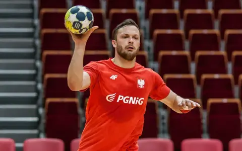 Mateusz Przybylski w czerwonej koszulce z orłem i logo PGNiG, gotowy do rzutu piłką ręczną.