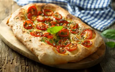 Pyszna focaccia z pomidorkami koktajlowymi i bazylią. Idealna jako dodatek do dań lub samodzielna przekąska. Z czym jeść focaccię? Z wszystkim, co lubisz!