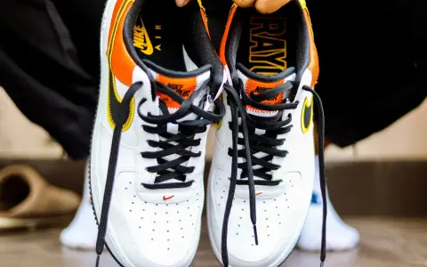 Białe buty Nike Air Force 1 z pomarańczowo-żółtymi akcentami. Sprawdź metkę i logo, by dowiedzieć się, jak sprawdzić czy buty są oryginalne.