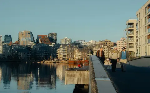 Promenad över bron i Oslo centrum med moderna byggnader och vatten.
