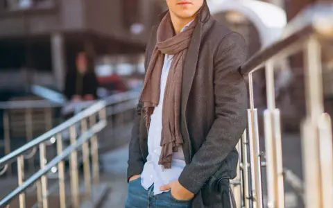 Uomo con cappotto grigio, camicia azzurra e pashmina marrone, un esempio di come indossare una pashmina in modo chic.