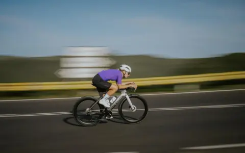Kolarz w fioletowej koszulce pędzi na rowerze, osiągając prędkość 50 km/h.