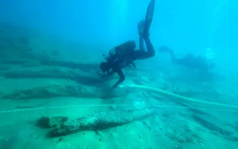 Subacquei esplorano un sito archeologico subacqueo, tra antichi resti di legno. Un'immersione per scoprire cosa vedere.