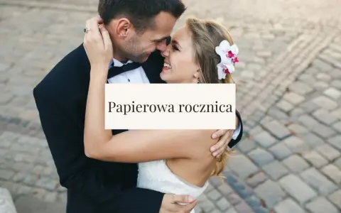 Para świętuje papierową rocznicę ślubu. Uśmiechnięci, w objęciach, z kwiatem we włosach panny młodej.