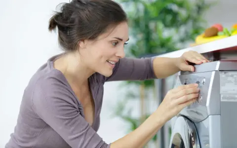 Lächelnde Frau stellt ein Programm an der Waschmaschine ein, um sie zu entkalken.