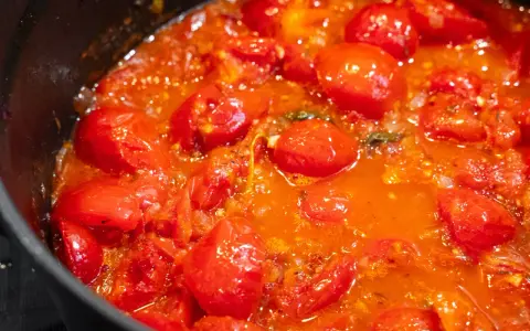 Ein köstliches, blubberndes Tomaten Sugo in einer schwarzen Pfanne, voller saftiger Kirschtomaten und aromatischer Kräuter.