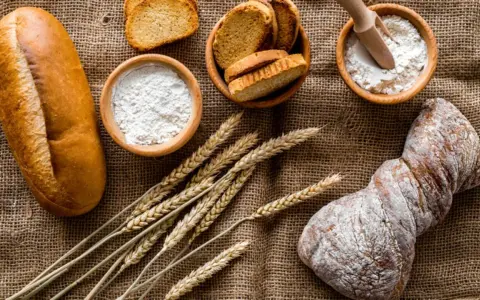 Brot, Getreideähren und Schalen mit Mehl, darunter Vollkornmehl aus Deutschland, liegen auf Jute.