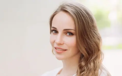 Uśmiechnięta kobieta z mysi blond włosami, delikatnie falującymi na ramionach.