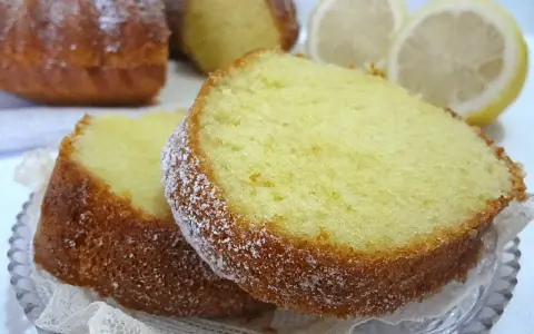 Fette di ciambellone al limone spolverate di zucchero a velo, con fette di limone sullo sfondo.
