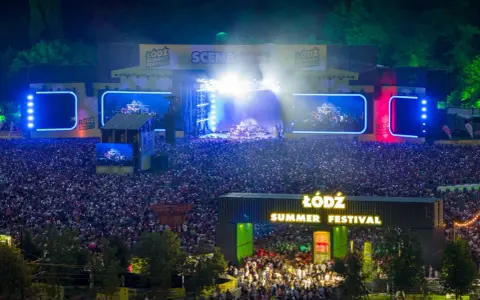 Tłum ludzi na koncercie podczas Łódź Summer Festival 2026. Na scenie gra zespół, a widzowie oświetlają teren telefonami.