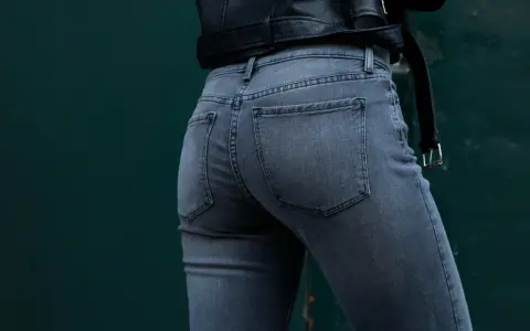 Vue arrière d'une femme portant un jean gris à coupe ajustée, avec une veste en cuir noir.