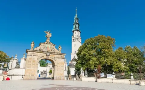 Brama na Jasną Górę, gdzie pielgrzymi zastanawiają się, ile ma lat to miejsce o bogatej historii. Wieża klasztoru góruje nad zielenią.