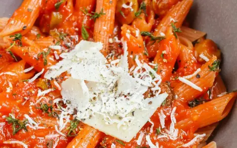 Szybki obiad z makaronem penne w sosie pomidorowym, posypany parmezanem i ziołami. Idealny na szybki posiłek.