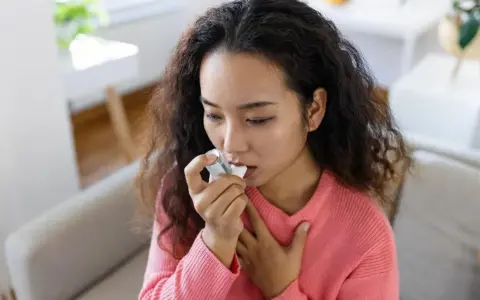 Junge Frau mit Asthma benutzt ihren Inhalator, der Cortison enthält, um ihre Atemwege zu öffnen.
