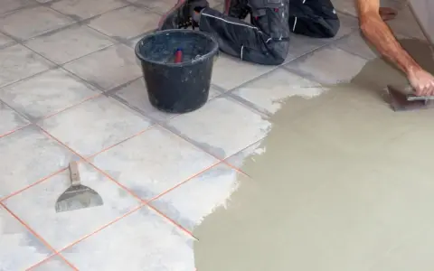 Hand verputzt Fliesen mit Spachtel und Mörtel. Ein Eimer und Werkzeug liegen bereit.