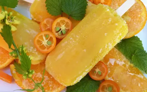 Paletas de helado de naranja, rodajas de naranja y kumquats adornan esta refrescante escena veraniega.
