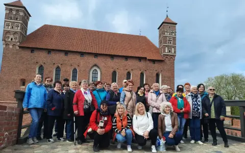 Grupa turystek pozuje na tle imponującego zamku biskupów warmińskich w Lidzbarku Warmińskim.