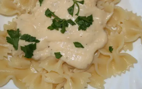 Makaron farfalle polany kremowym sosem serowym i posypany natką pietruszki.