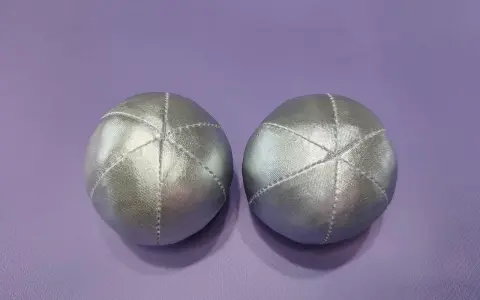 Deux balles en tissu argenté, parfaites pour un **patron gratuit balle en tissu**. Elles sont posées sur un fond violet.