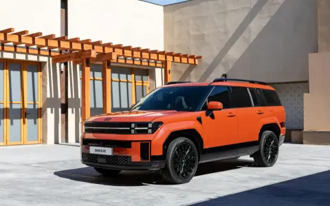 Pomarańczowy Hyundai Santa Fe, jeden z najlepszych SUV-ów, parkuje przed nowoczesnym budynkiem z drewnianą pergolą.