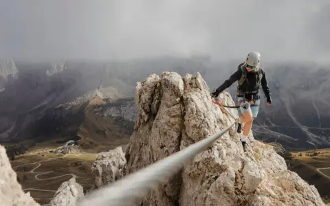 Kobieta w kasku i uprzęży pokonuje via ferrata, czyli ubezpieczoną trasę w skałach. Widok zapiera dech w piersiach!