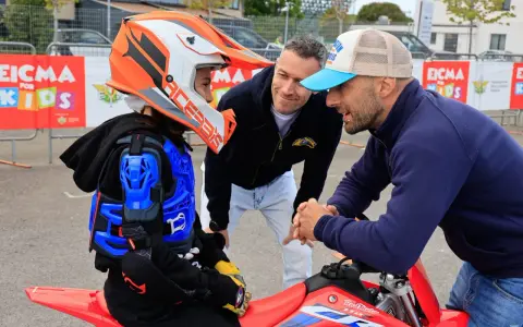 Giovane motociclista donna con casco e protezioni, ascolta i consigli di due uomini.