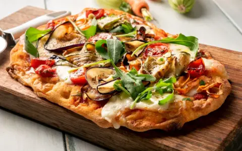 Chrupiący spód do pizzy z bakłażanem, cukinią i pomidorkami, posypany rukolą i mozzarellą.