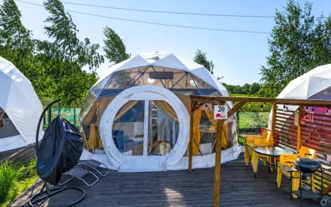 Nowoczesne namioty sferyczne na energylandia pole namiotowe. Drewniany taras z grillem i żółtymi krzesłami.