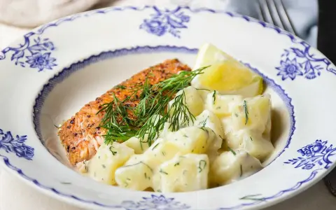 En bit stekt lax med citron och en generös portion krämig dillstuvad potatis, serverad på en vacker blåvit tallrik.