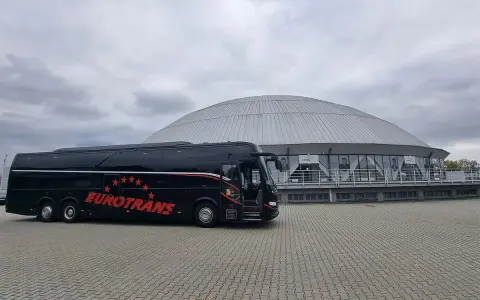 Czarny autokar turystyczny "Eurotrans" przed nowoczesnym budynkiem z kopułą.