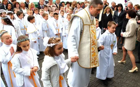 Dzieci w białych strojach, kiedy jest komunia, idą z księdzem.