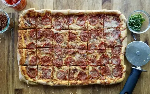 Domowa pizza na blachę z pepperoni, posypana parmezanem. Idealna na rodzinne spotkanie.
