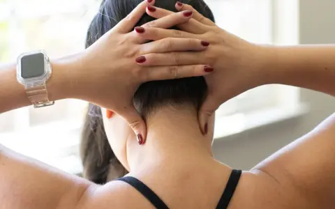 Hands demonstrate shiatsu self neck massage techniques, applying pressure to the base of the skull and sides of the neck.