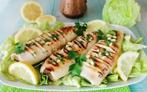 Tre calamari alla griglia, conditi con aglio e prezzemolo, serviti su un letto di lattuga con spicchi di limone.