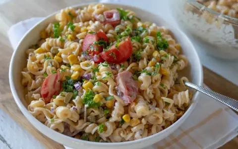 Pyszna sałatka z makaronem fusilli, kukurydzą, pomidorami i natką pietruszki, polana kremowym sosem. Idealna na letnie dni.