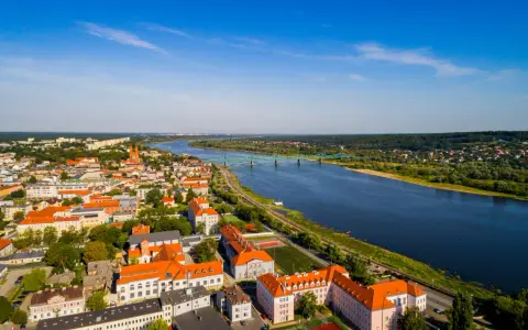 Widok z lotu ptaka na miasto nad Wisłą, z zielonym mostem i zabudowaniami w słoneczny dzień.