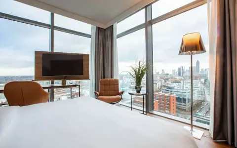 Modern Hotelzimmer mit Skyline-Blick, Bett, Sessel und Fernseher.
