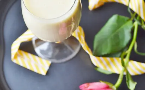 Kremowy likier bananowy w kieliszku, ozdobiony żółto-białą wstążką. Idealny na deser, jak z przepisu na likier bananowy.